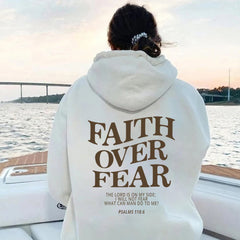 Woman wearing a Faith Over Fear Hoodie by the water, featuring an inspirational quote and motivational design.